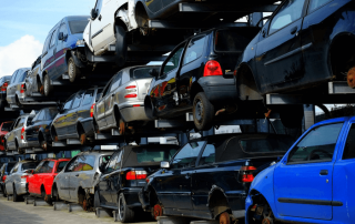 An image of a car scrap yard, with vehicles stacked on top of one another.